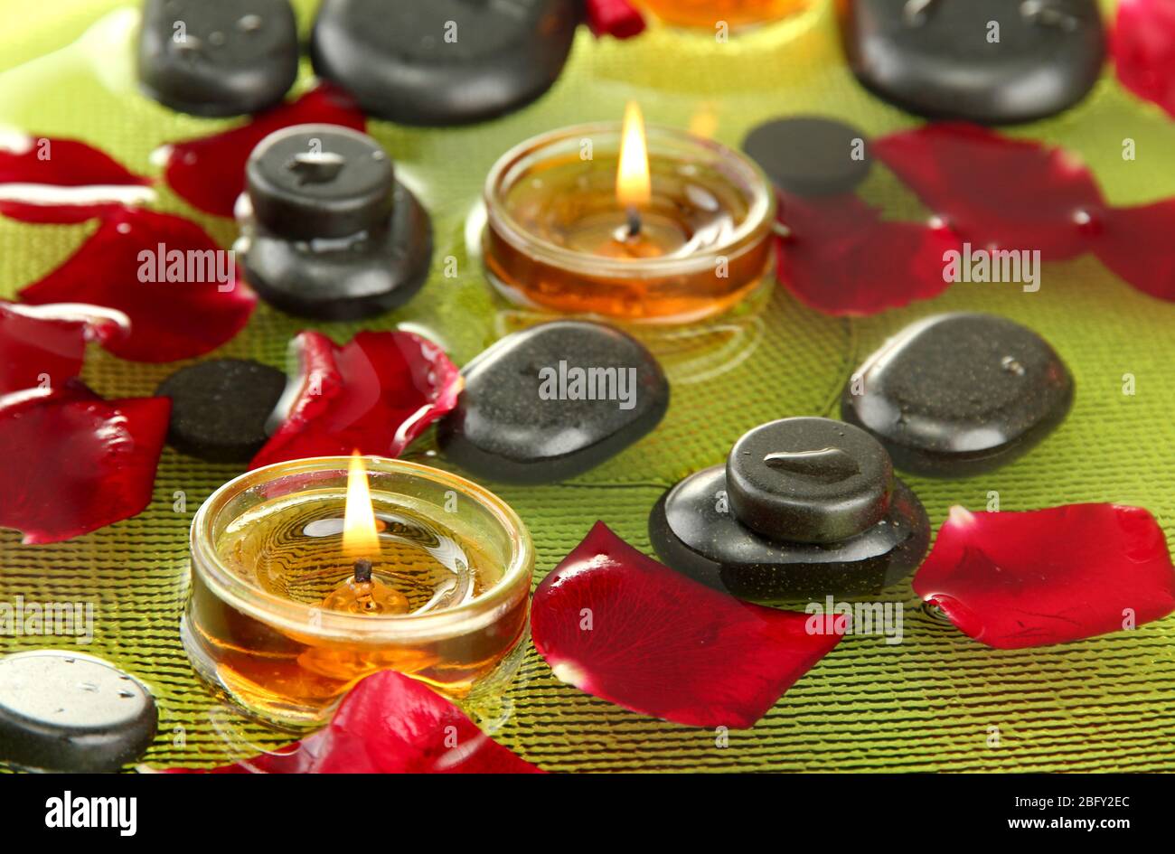 spa stones with rose petals and candles in water on plate Stock Photo ...