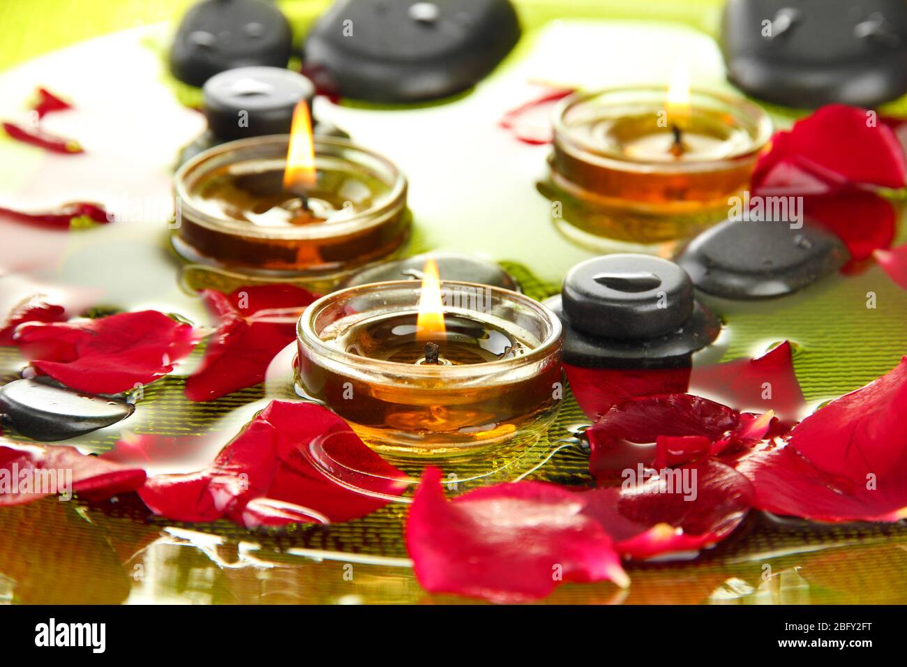 spa stones with rose petals and candles in water on plate Stock Photo ...