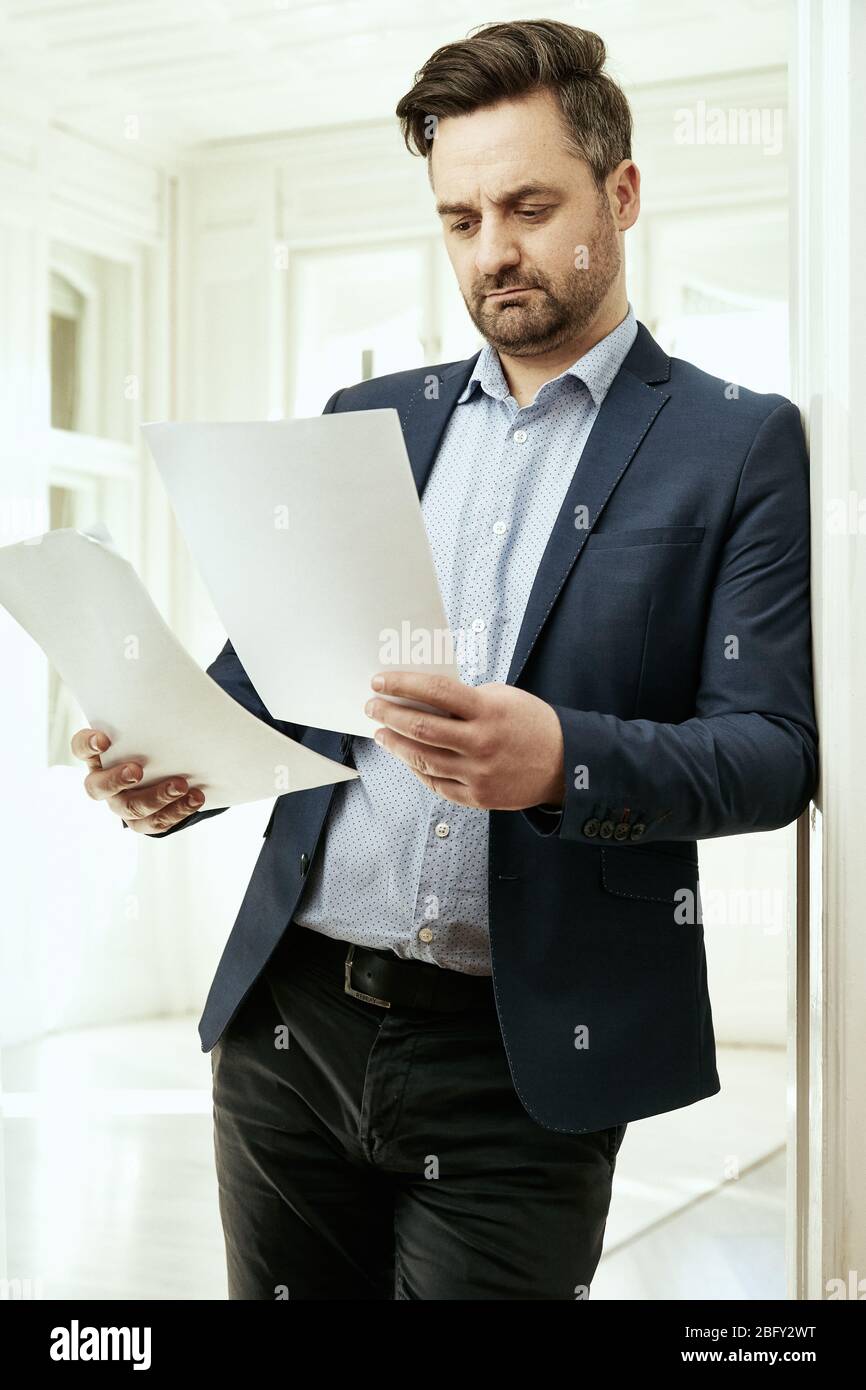 A businessman is reading. He is holding papers in his hands. Office, home office. Stock Photo