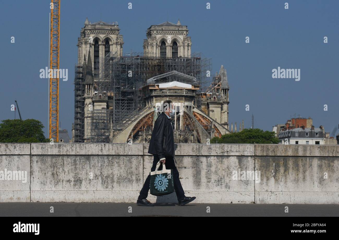*** STRICTLY NO SALES TO FRENCH MEDIA OR PUBLISHERS - RIGHTS RESERVED ***April 12, 2020 - Paris, France: Parisians wearing protection masks against the coronavirus walk by Notre Dame cathedral on Easter. All restoration work has been stopped during the lockdown. A devastating fire took place on April 15, 2019. A year later, Paris is struggling against the Covid-19 outbreak. Stock Photo