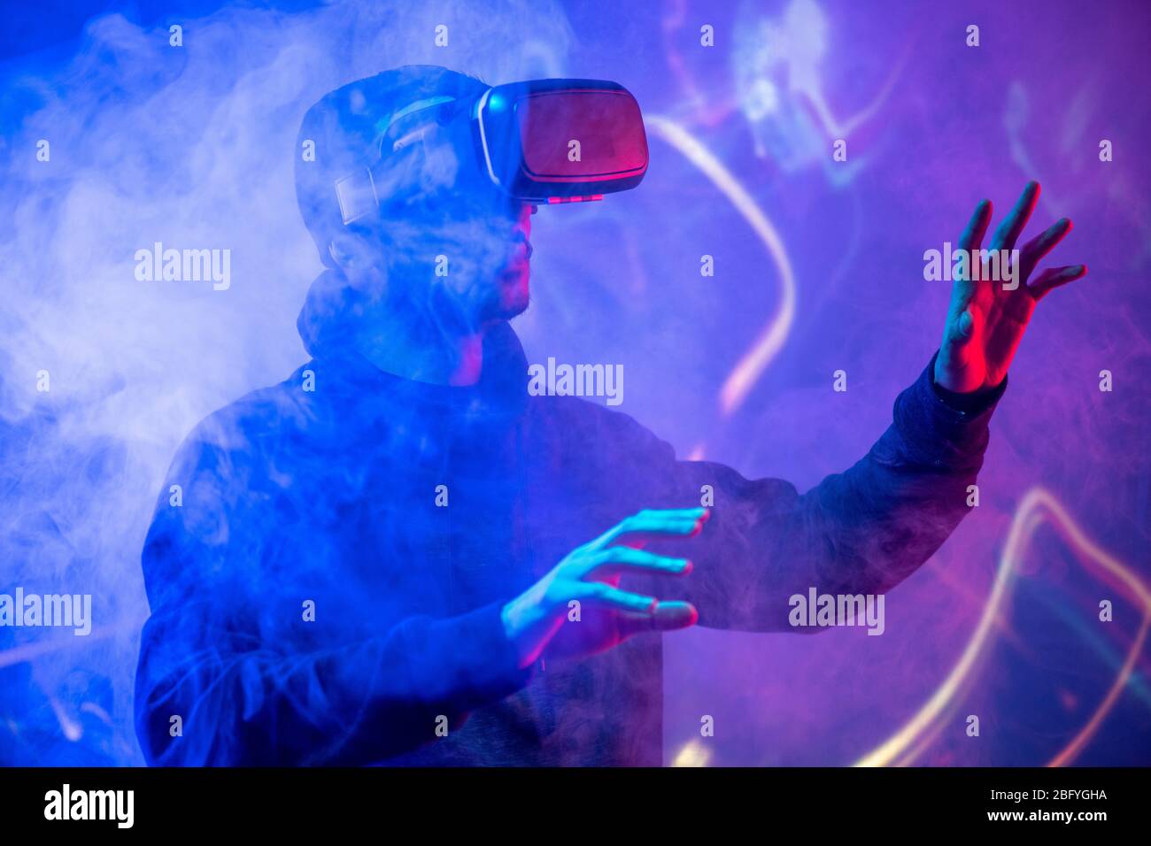 Young Arabian man using virtual reality device gesturing hands in smoked VR room Stock Photo