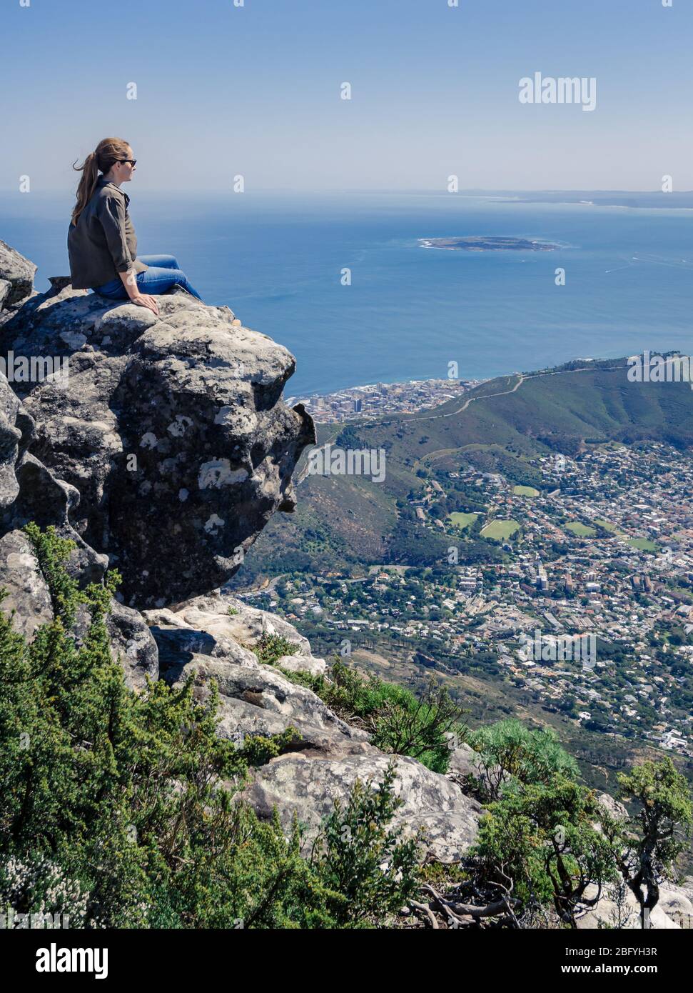 Woman sitting on cliff edge  overlooking ocean and Roben island from table mountain cape town south africa Stock Photo