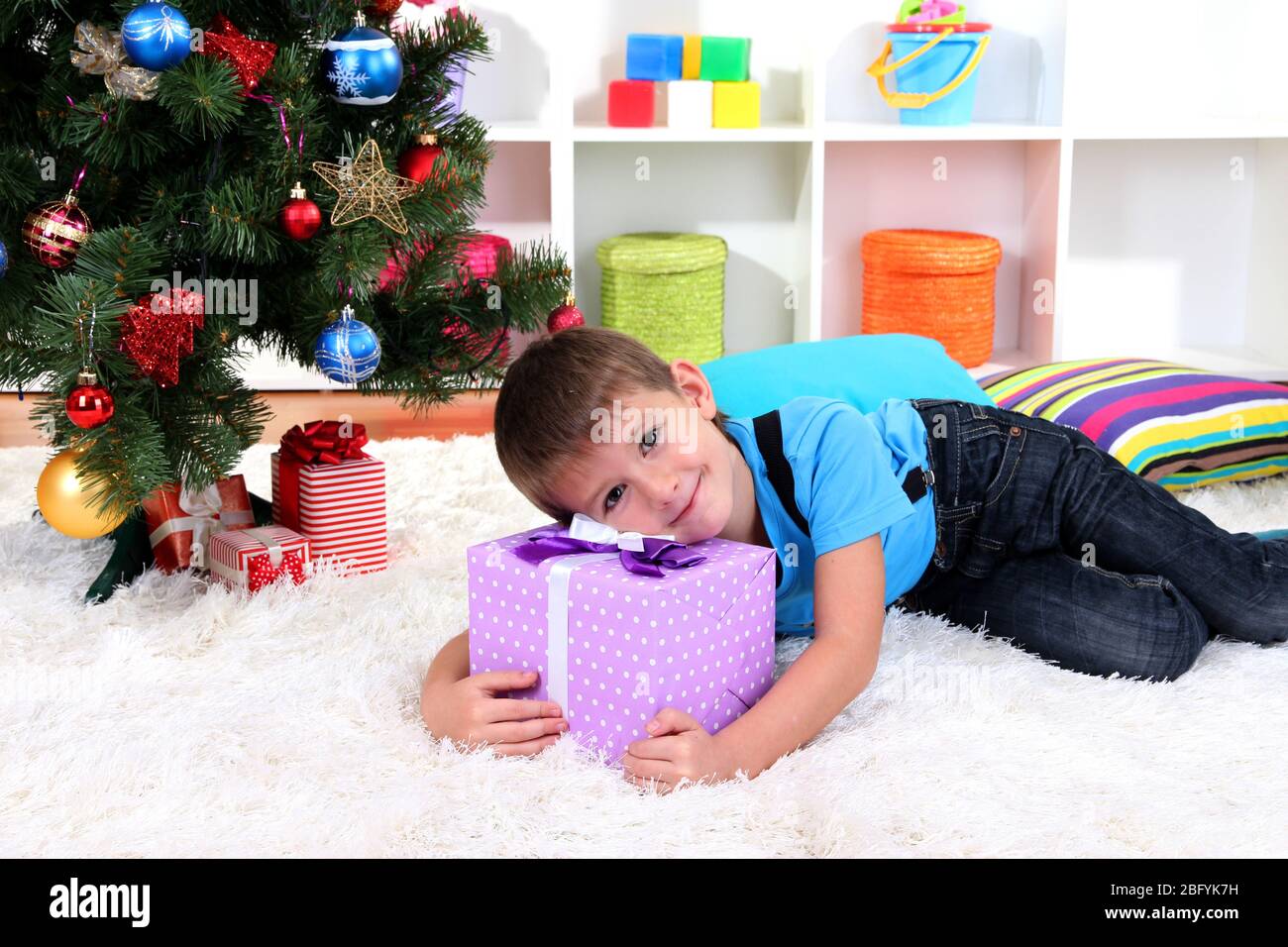 Little boy lying on gift in his hands under Christmas Tree waiting for