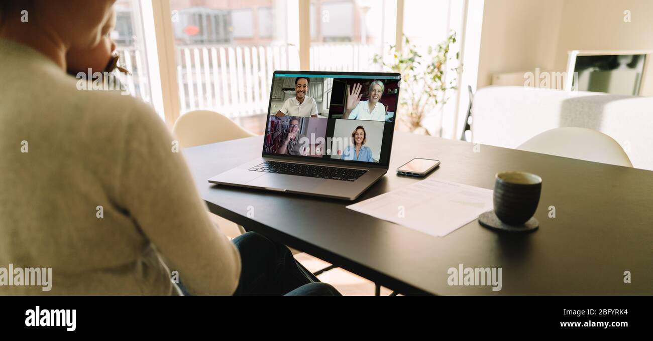 Business team meeting online over a video call on laptop. Woman sitting at table at home having a video conference with her colleagues. Stock Photo