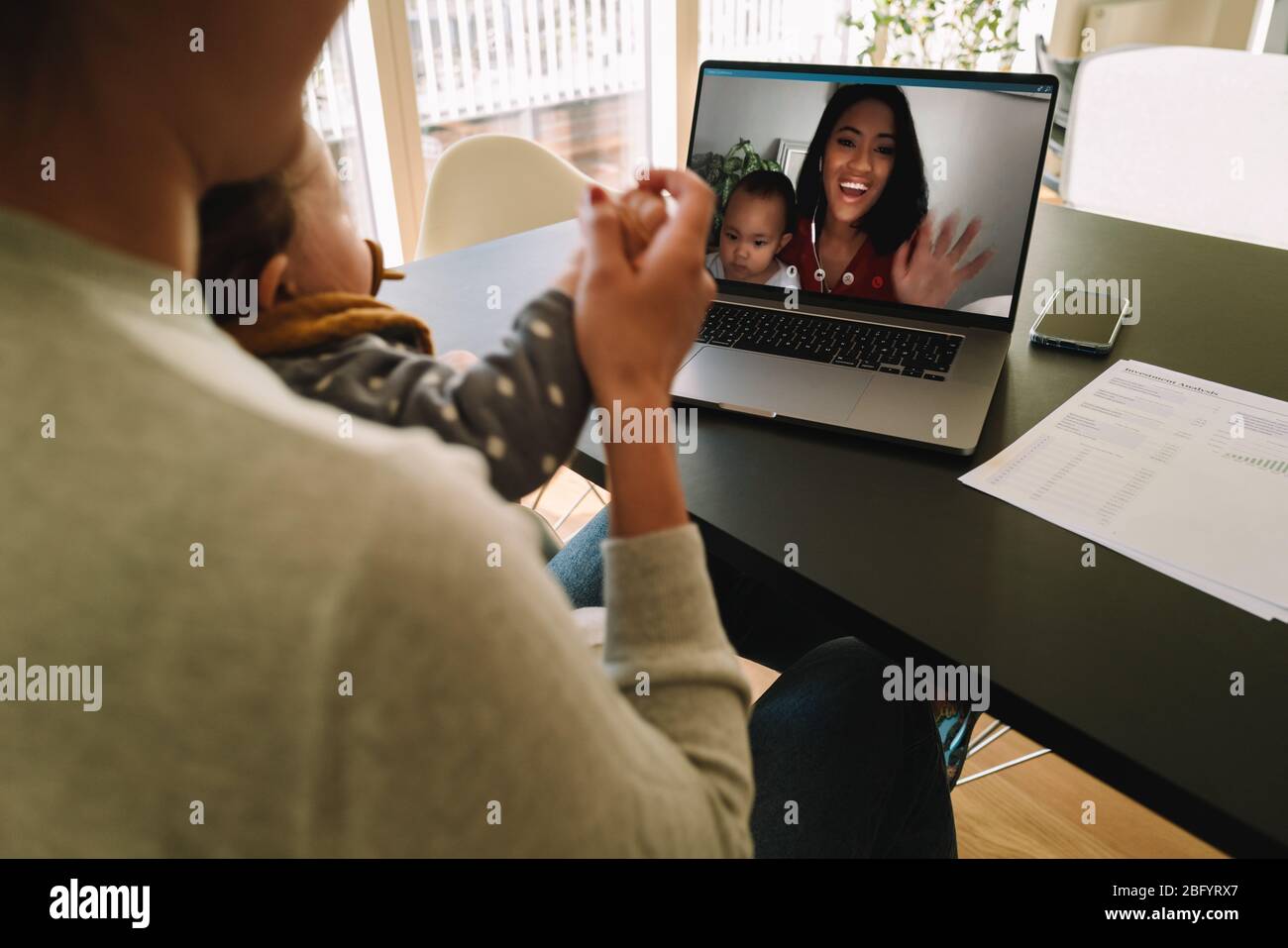 Woman using a laptop to connect with her sister during quarantine. Female friends with their kids having a video call on a laptop computer at home. Stock Photo