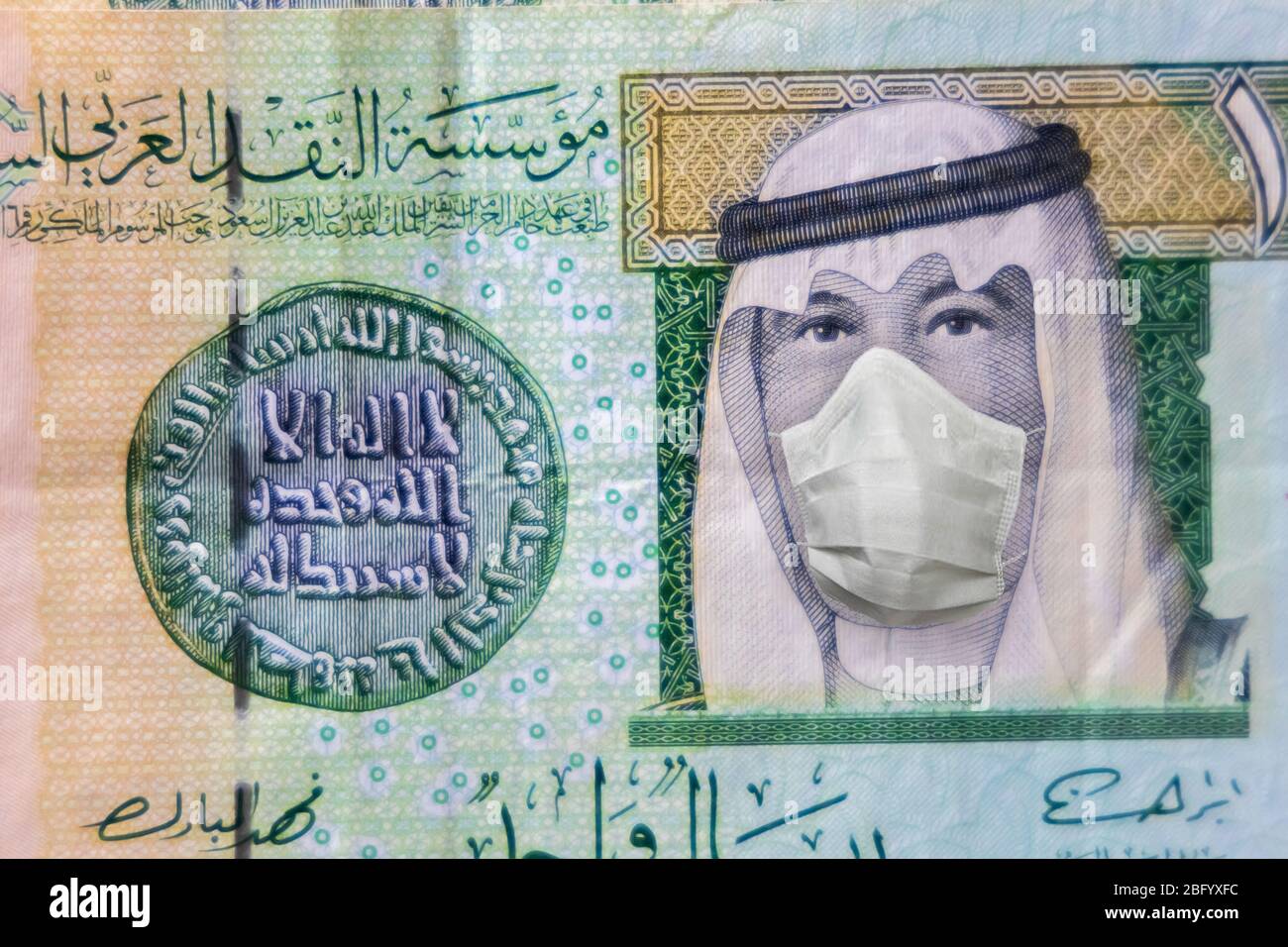 COVID-19 coronavirus in Gulf, 1 Riyal money bill with face mask. Coronavirus affects global stock market. World economy hit by corona virus outbreak a Stock Photo