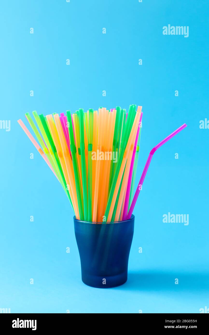 Colorful plastic drinking straws in glass container on light blue