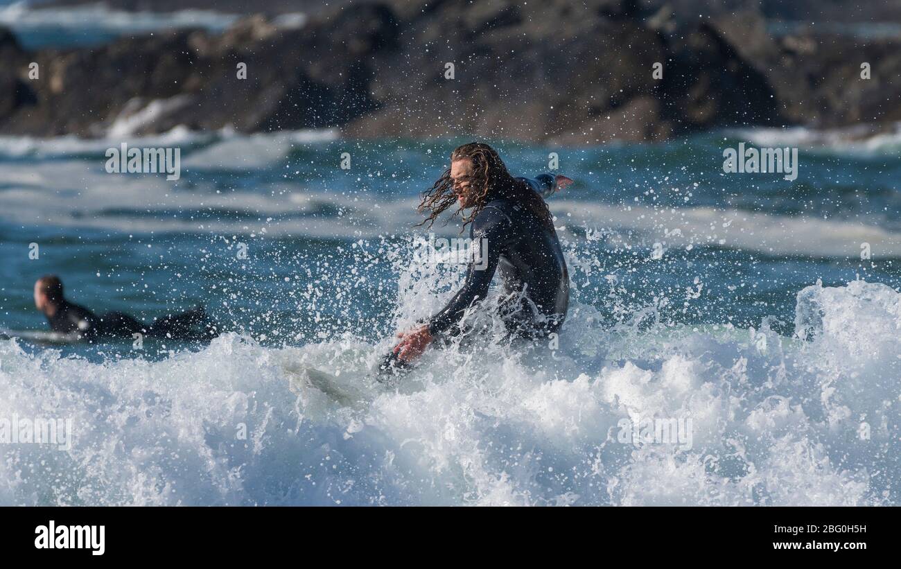 A panoramic image of a male surfer with long hair riding a wave at Fistral in Newquay in Cornwall. Stock Photo