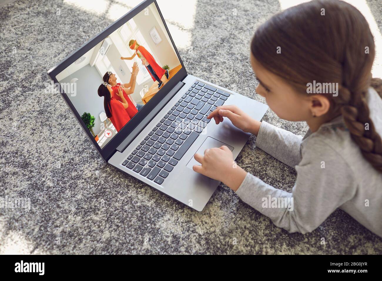 A child uses a laptop to watch home videos in a room on the floor. Stock Photo