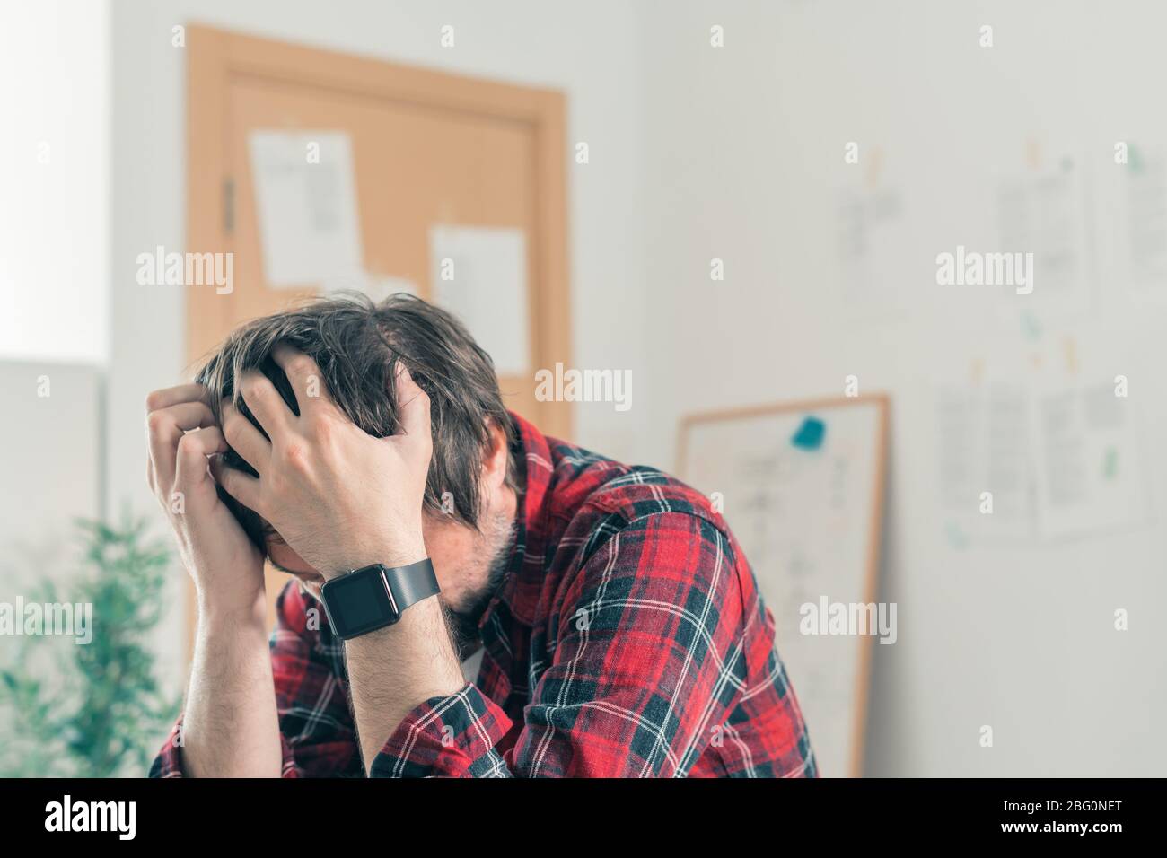 Disappointed freelancer at home office with his head in hands, selective focus Stock Photo