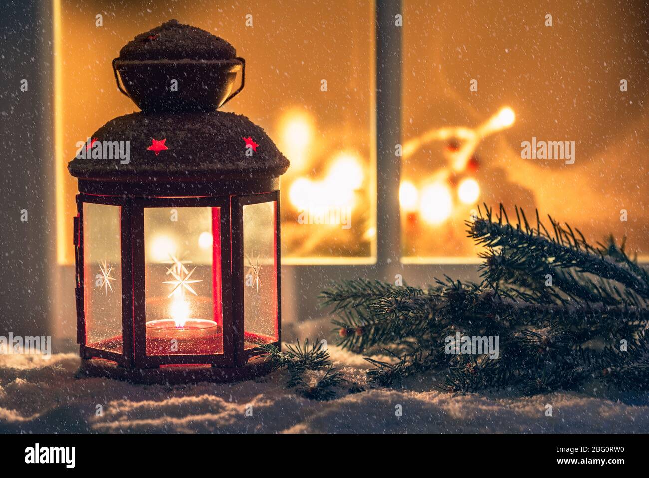 Clse up of  a lit Christmas lantern on an external windowsill covered in snow on a snowing night. Copy space. Stock Photo