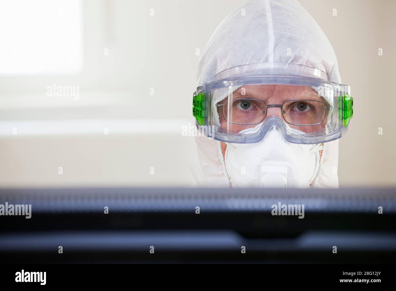 Face of a tired doctor with protective clothing an medical mask behind a computer monitor in a hospital - selective focus Stock Photo