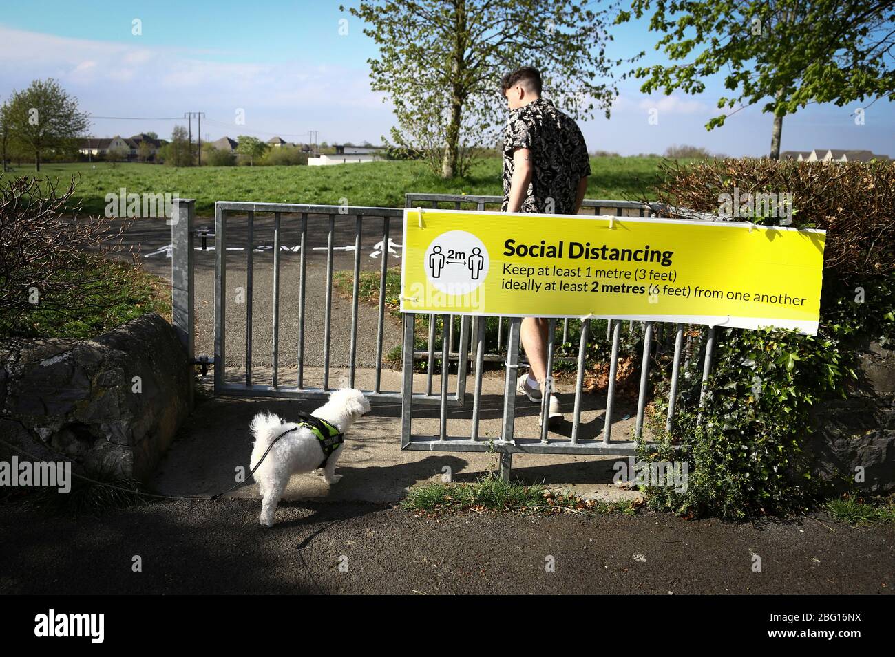 Dublin, Ireland - April 19, 2020: a jogger passing a two metres social distancing public health notice in a park in the city centre. Stock Photo