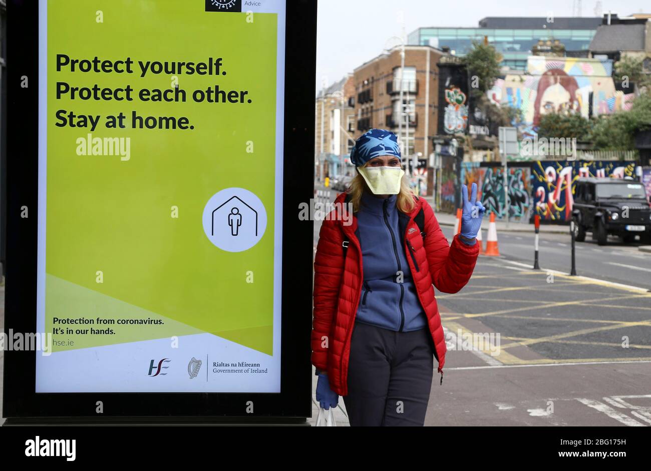 Dublin, Ireland - April 19, 2020: a woman wearing a face mask gives a peace sign while waiting for a bus in the city centre. Stock Photo