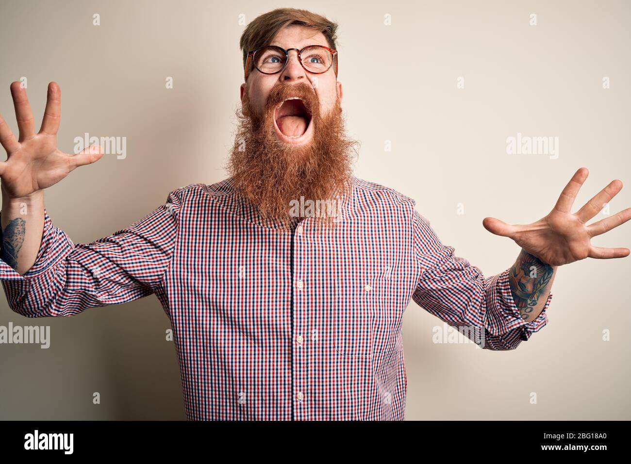 Handsome Irish redhead business man with beard wearing glasses over isolated background crazy and mad shouting and yelling with aggressive expression Stock Photo