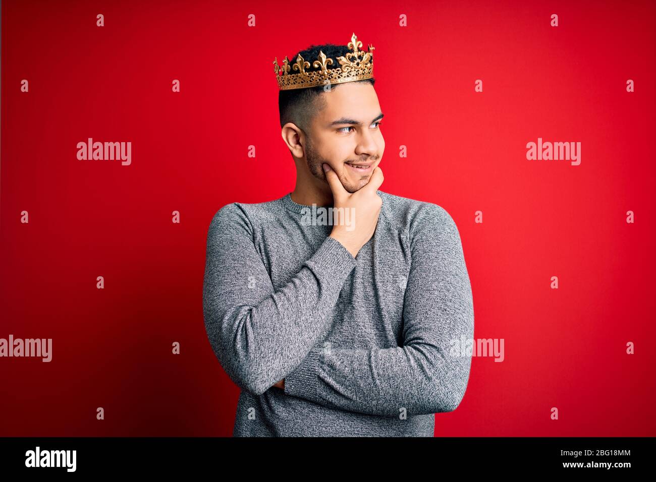 Young handsome man wearing golden crown of prince over isolated red ...