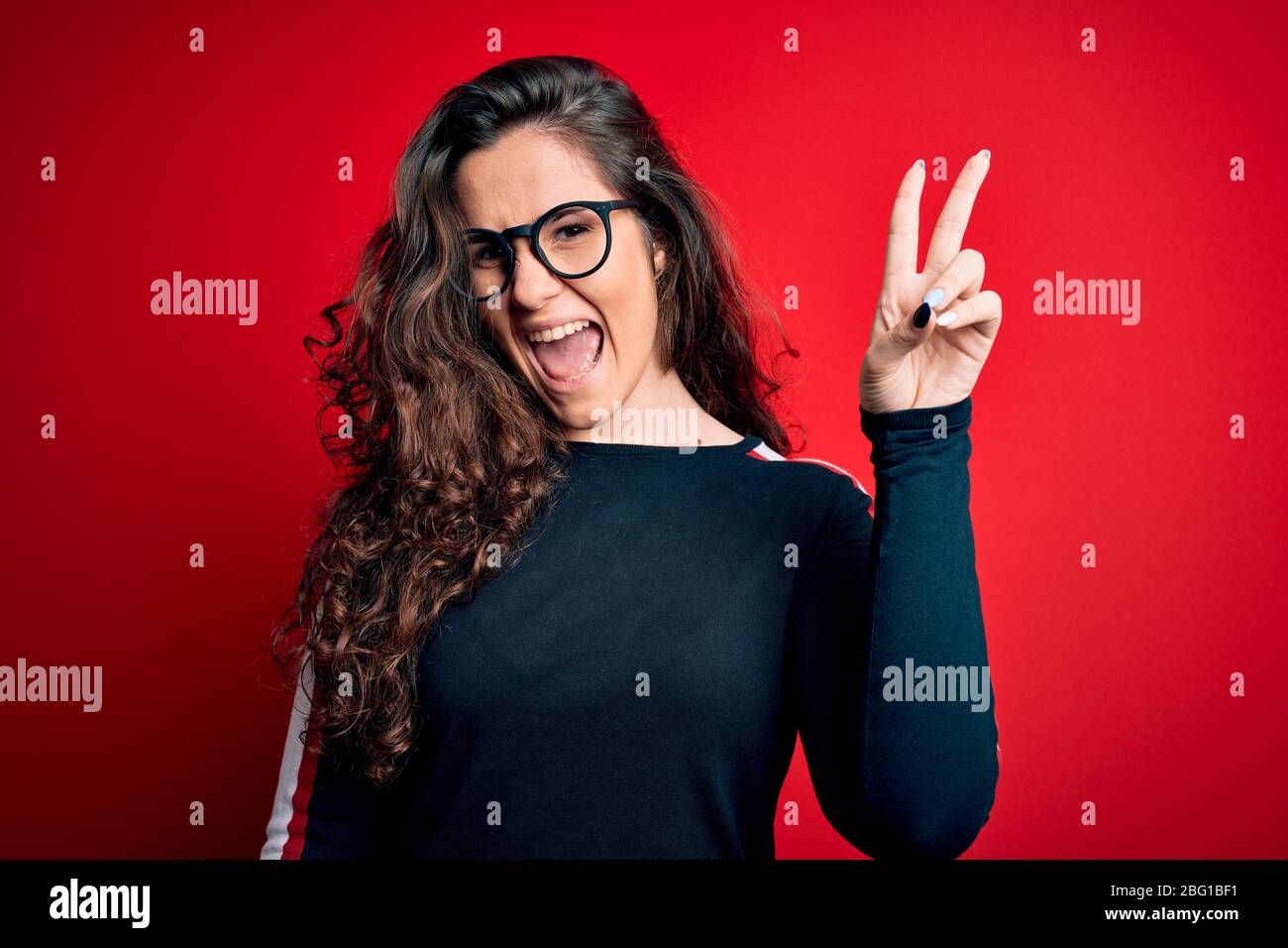 Young beautiful woman with curly hair wearing sweater and glasses over ...