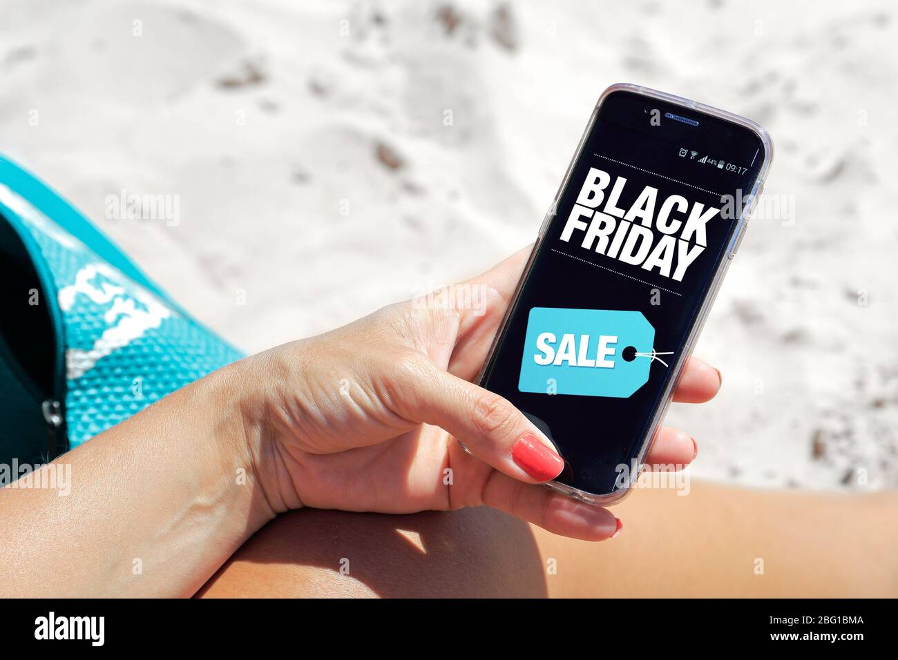 Woman on the beach with a cell phone in her hands. You can see a Black Friday advertising on the screen. Marketing, ecommerce, cell phone publicity. Stock Photo