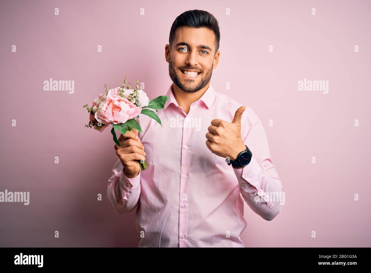 Young romatic man holding bouquet of spring flowers over pink isolatd ...