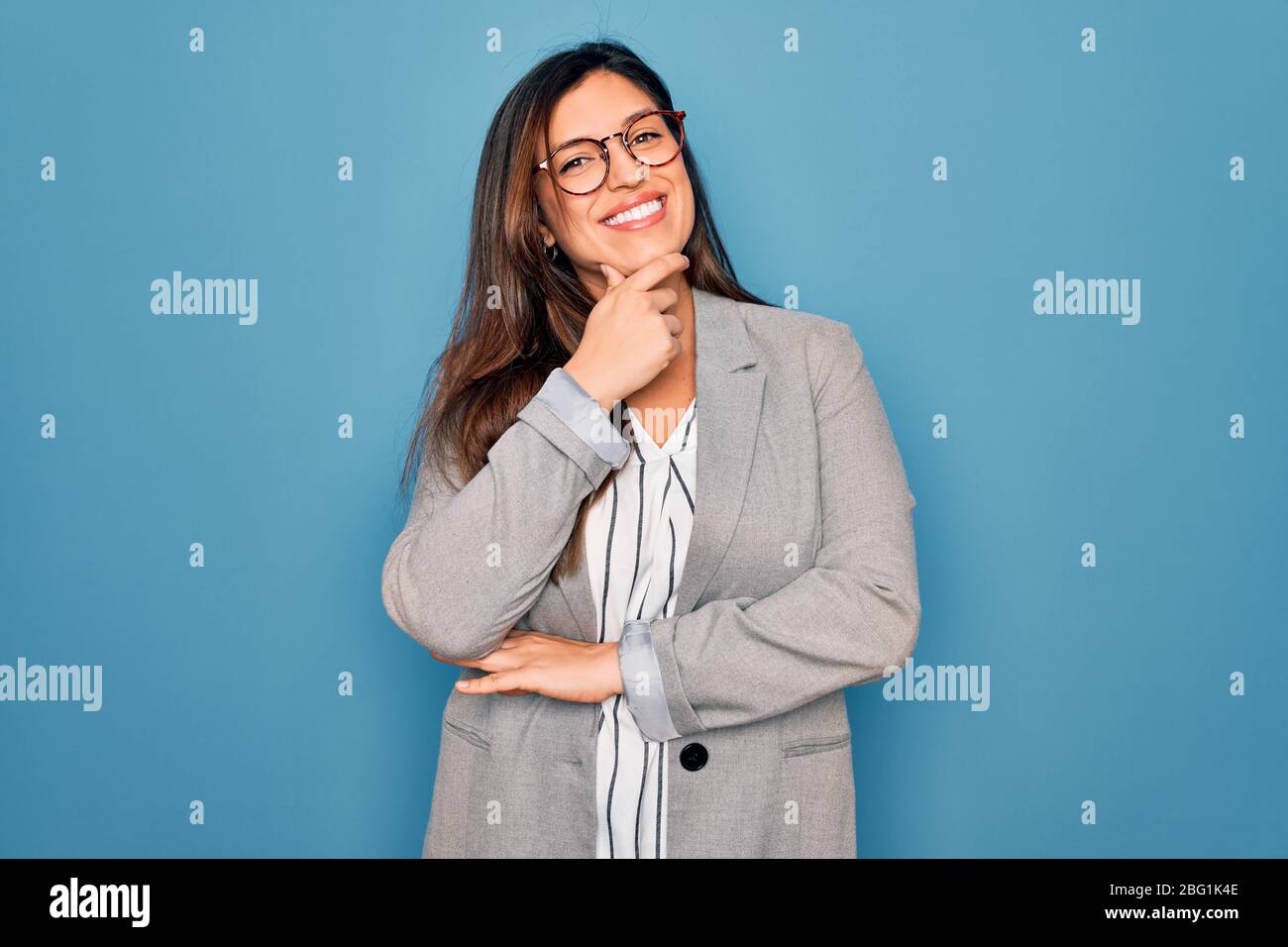 Young hispanic business woman wearing glasses standing over blue ...