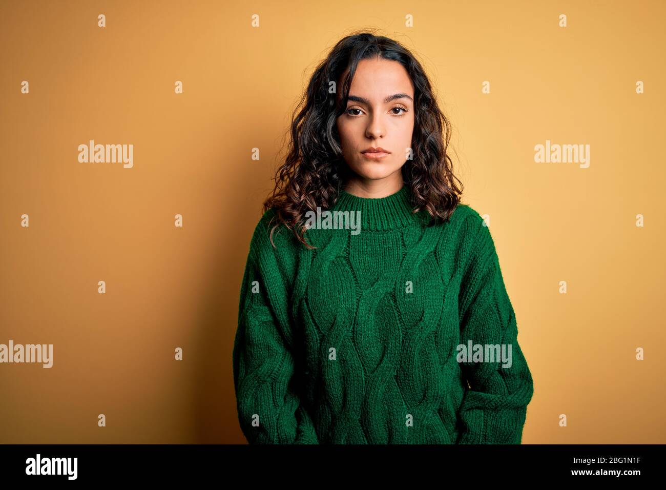 Young beautiful woman with curly hair wearing green casual sweater over ...