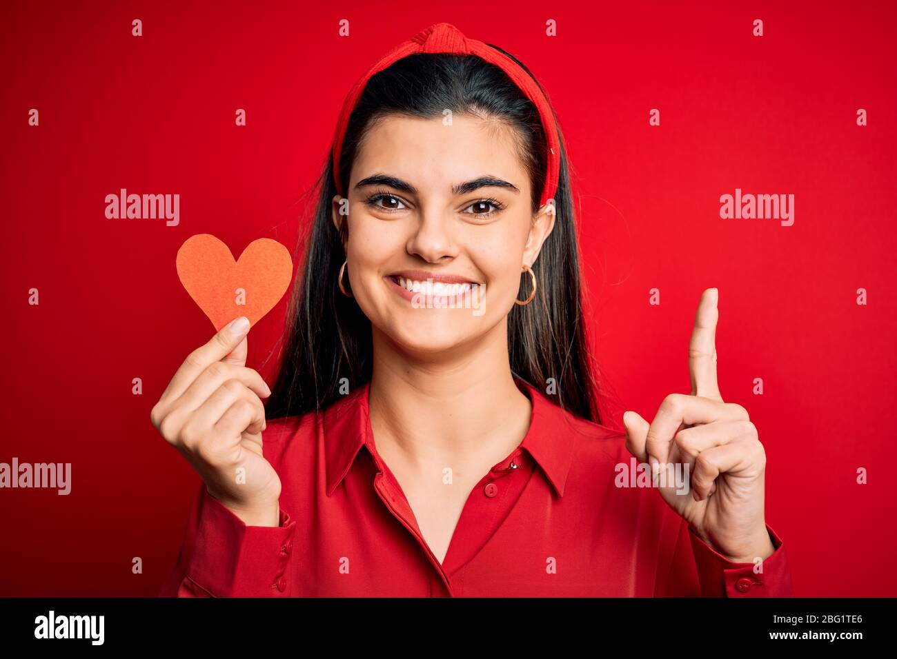 Young beautiful brunette romantic woman holding red heart paper for ...