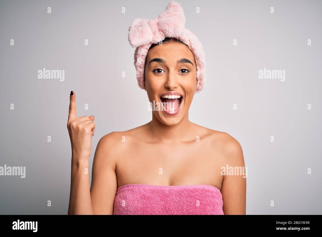 Young beautiful brunette woman wearing towel after shower over isolated white background pointing finger up with successful idea. Exited and happy. Nu Stock Photo