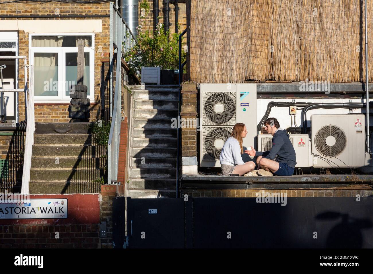 A young couple sits in the sun outside their flat in Brixton, during the London lockdown due to the spread of Covid-19, 19 April 2020 Stock Photo