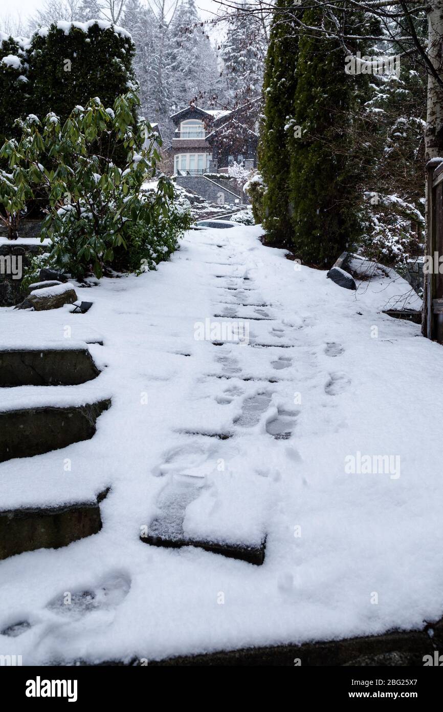 Footprints in the snow leading up a path beside a home in the winter. Stock Photo