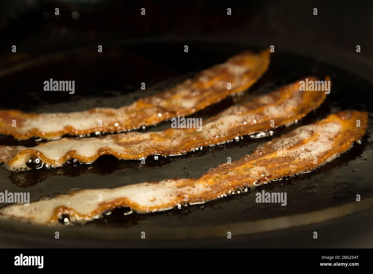 Closeup of some tasty strips of bacon frying in a pan. Stock Photo