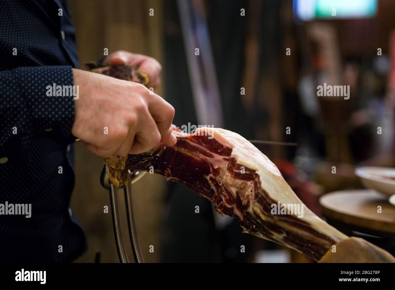 Closeup of a mans hand with a carving knife slicing of pieces of a serrano ham leg. Stock Photo