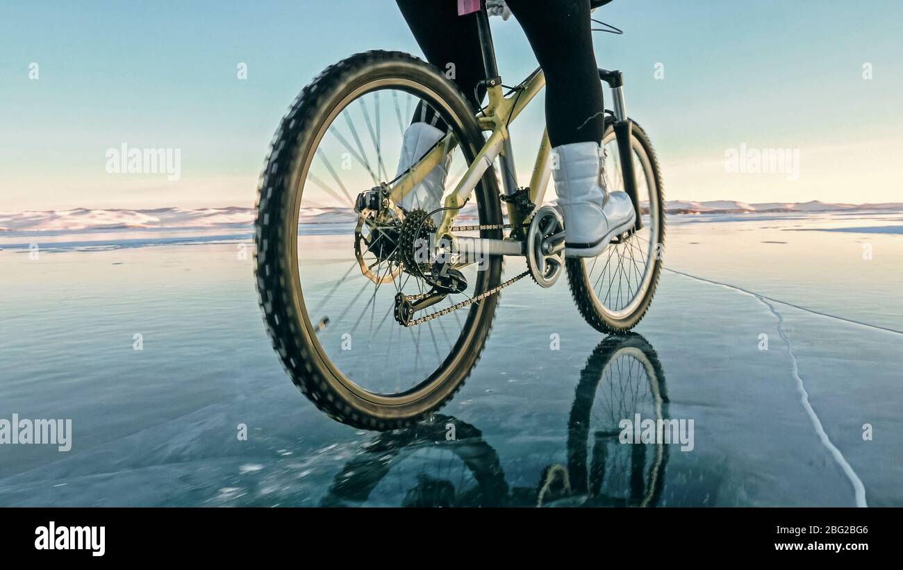 Woman is riding bicycle on the ice. Tires on bike are covered wi Stock