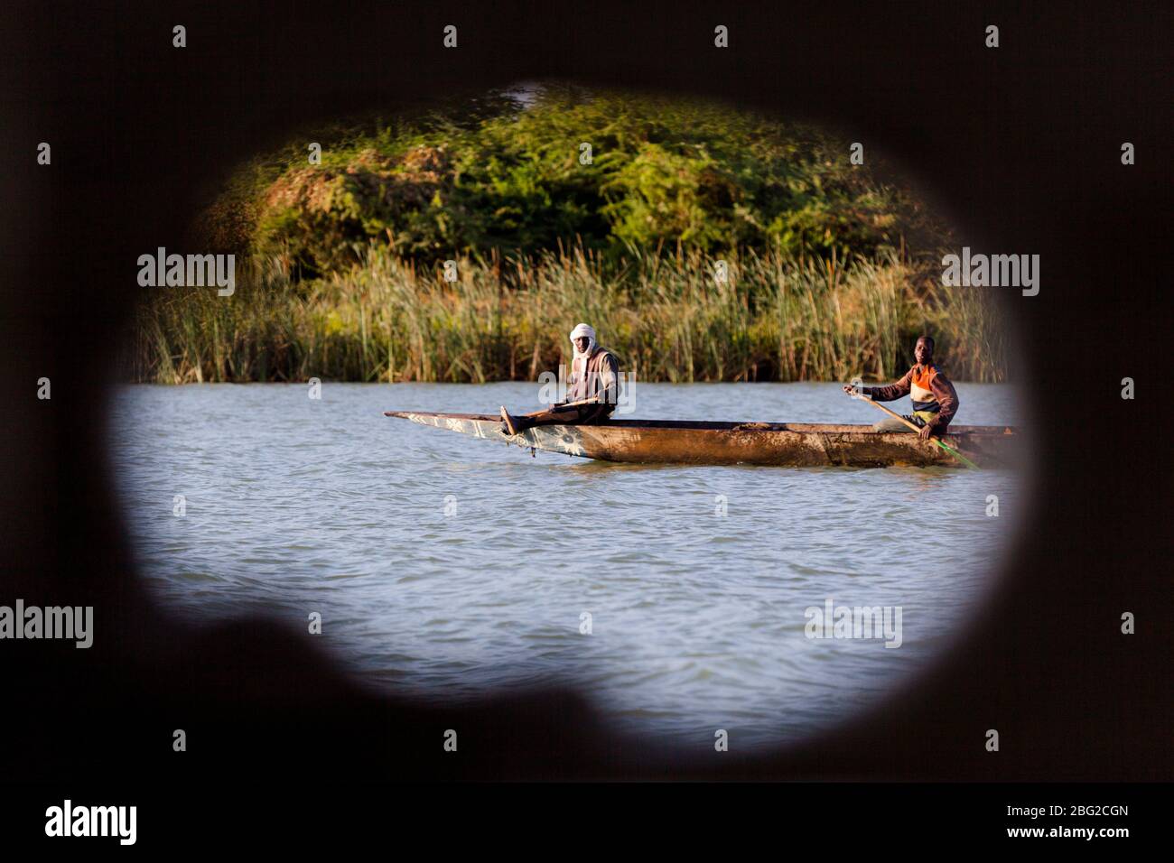 Senegal River locals paddling a pirogue as seen through a porthole on the Bou el Mogdad antique river boat. Stock Photo