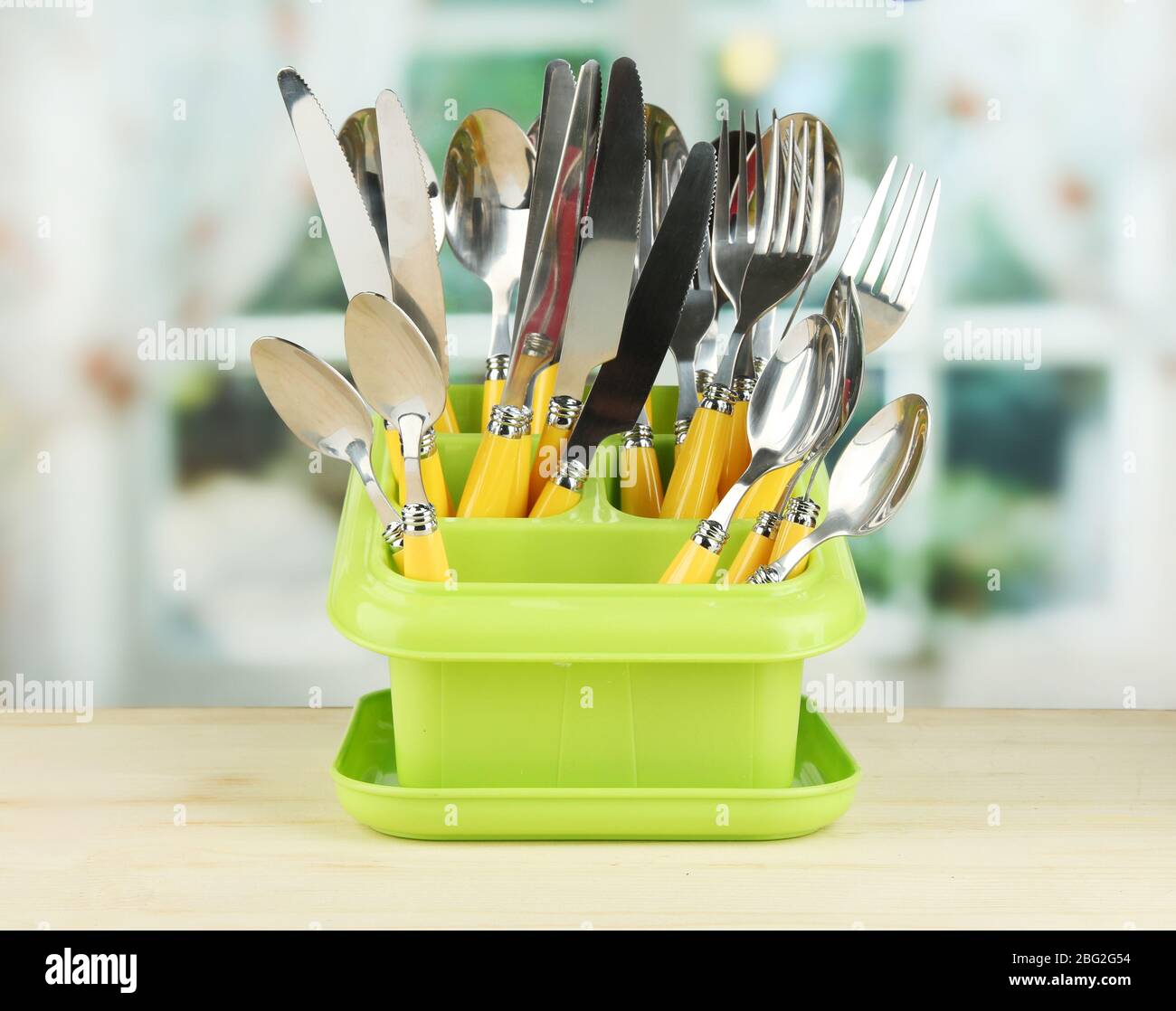 Knives, spoons, forks in plastic container for drying, on bright
