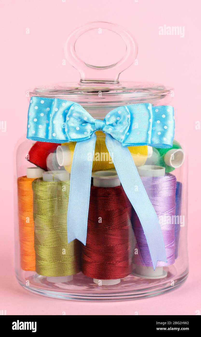 Glass jar containing various colored thread on pink background Stock ...