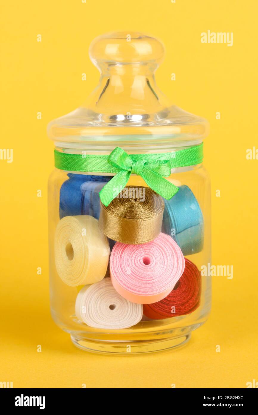 Glass jar containing various colored ribbons on yellow background Stock ...
