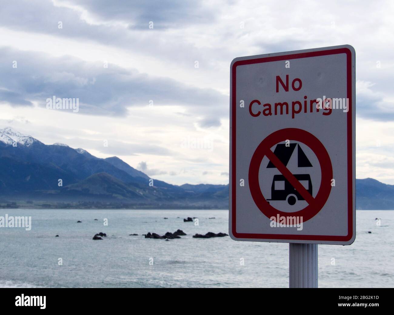 'No Camping' sign along the Esplanade in Kaikoura with mountains and beach in backdrop Stock Photo
