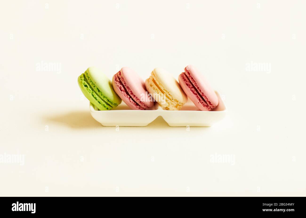 Minimal composition of delicious pastel-colored macaroons in row on china platter over white background, copy space Stock Photo