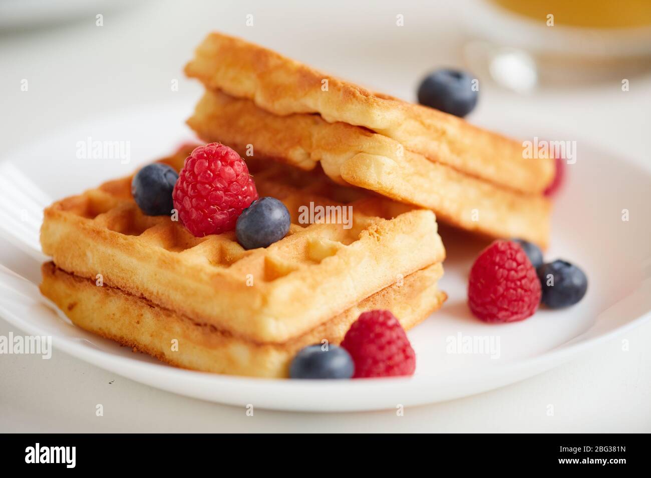 Minimal composition of sweet dessert waffles with berry topping laid over white plate on cafe table, copy space Stock Photo