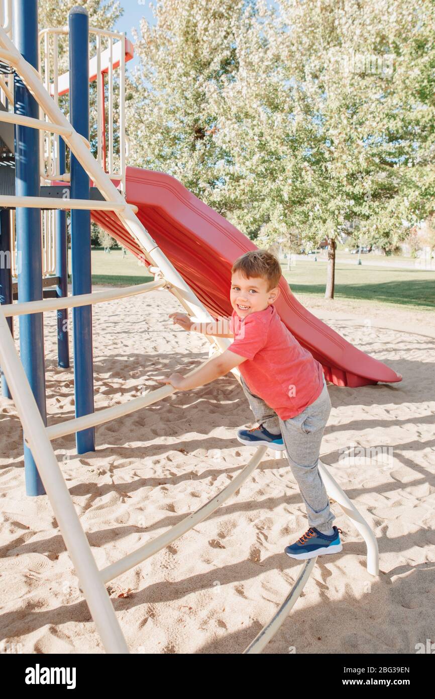 Active happy Caucasian boy climbing staircase climber on playground. Kid on schoolyard outdoors on summer sunny day. Child having fun outside on play Stock Photo
