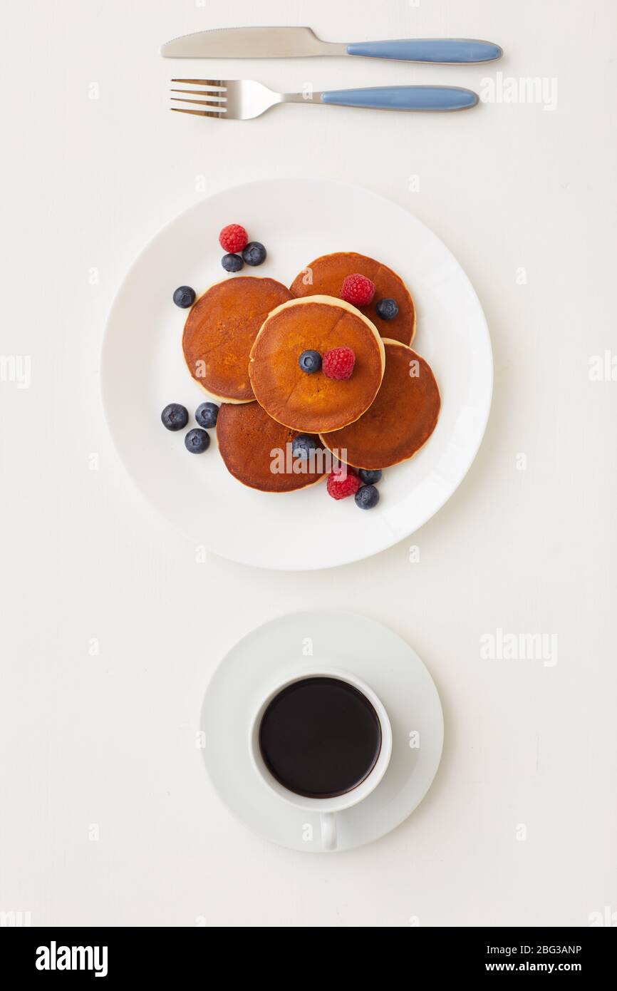 Top view at minimal composition of delicious golden pancakes decorated with fresh berries next to coffee cup on white background, breakfast concept, c Stock Photo