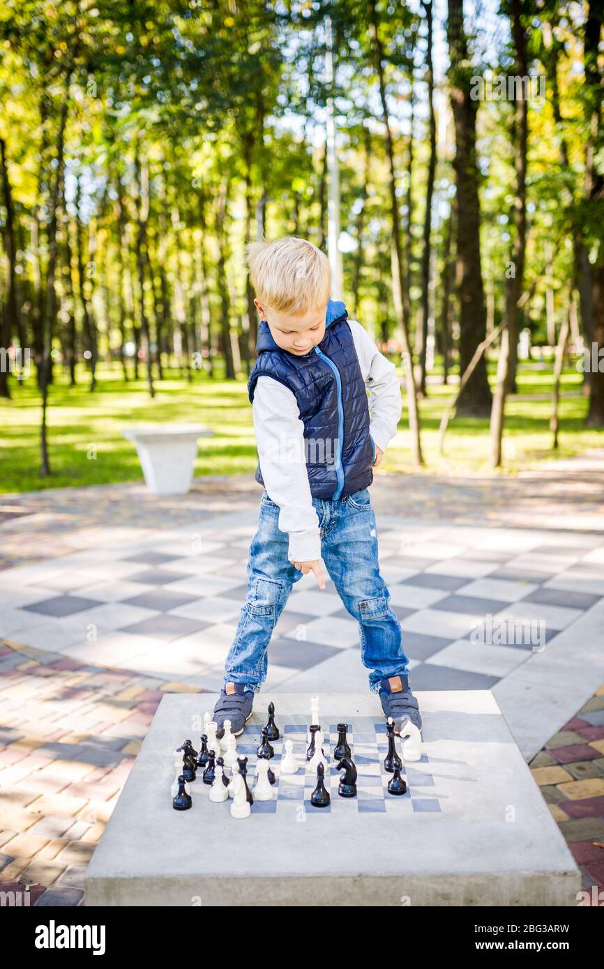 Child playing chess on board game outdoor. Hobby club children playing game chess with figures. Boys characters, childhood of personage, back to Stock Photo