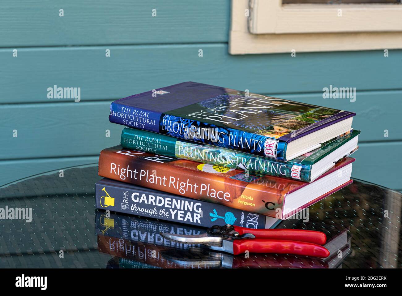 Garden books stacked on a table beside a summer house. Stock Photo