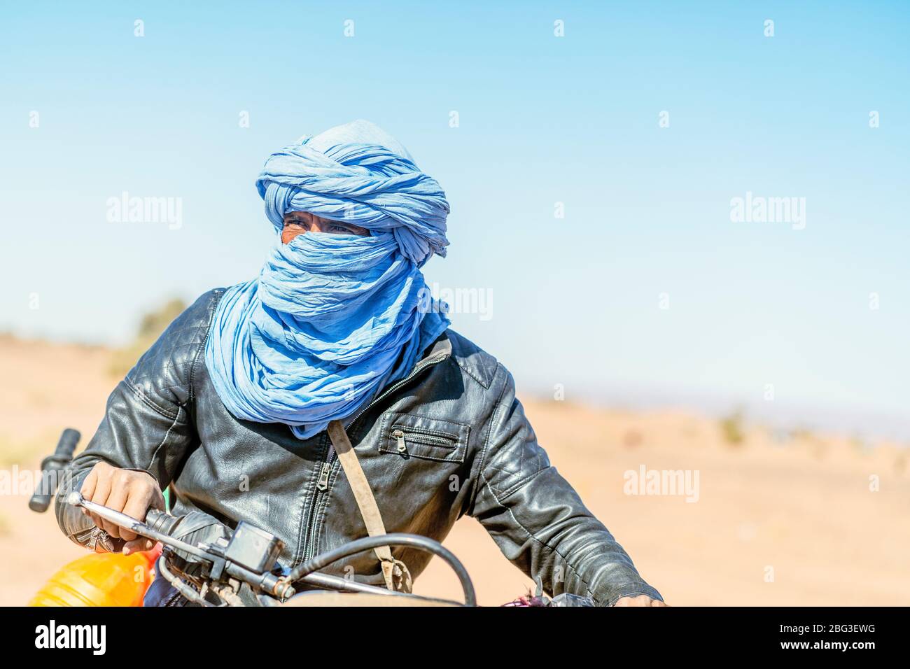 Mhamid, Morocco -  March 17, 2020: Amazing portrait of Bedouin man on his motorbike driving through Sahara Desert. Stock Photo