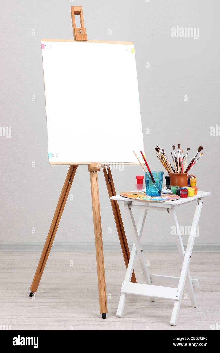 Wooden easel with clean paper and art supplies in room Stock Photo Alamy