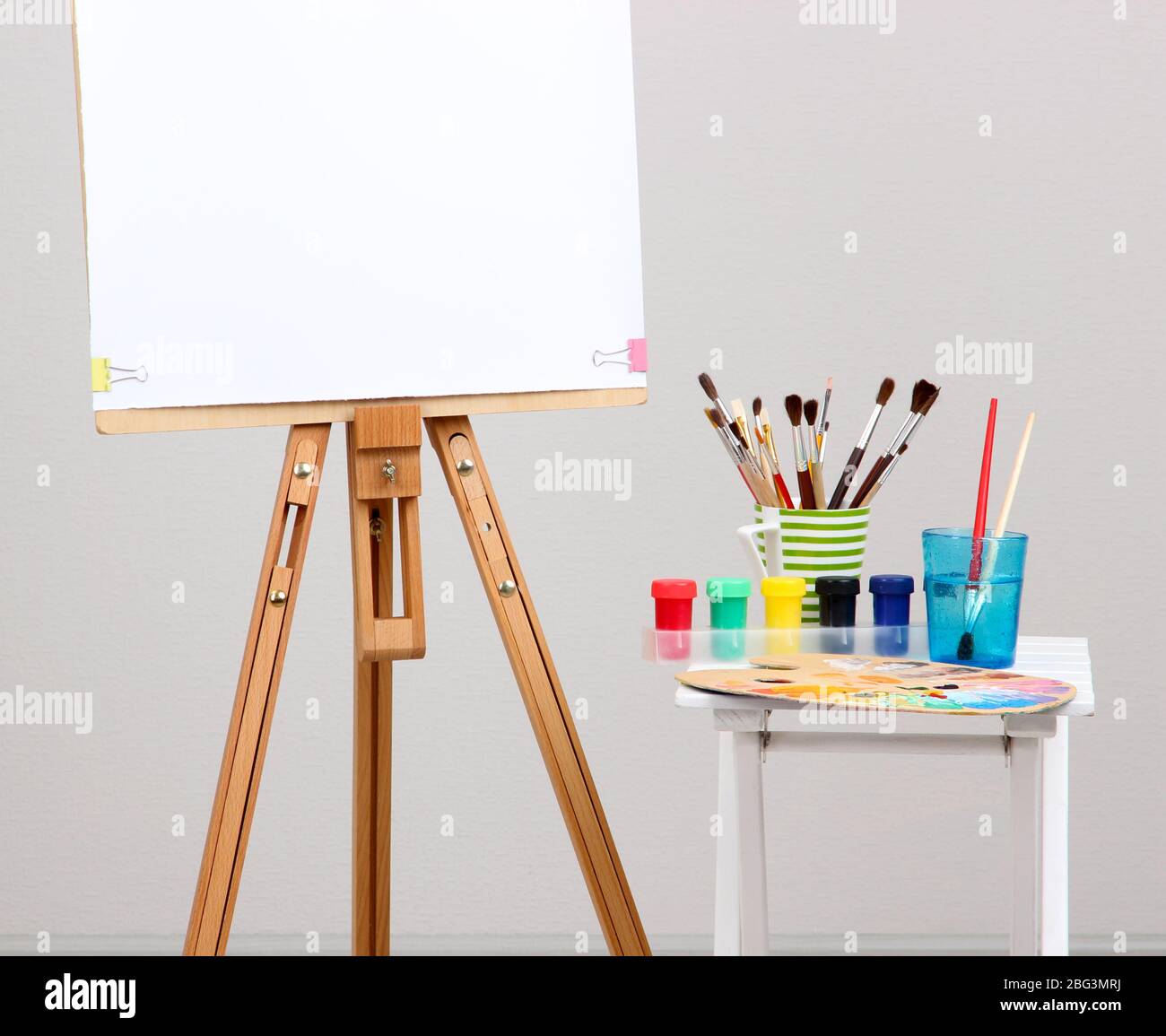 Wooden easel with clean paper and art supplies in room Stock Photo Alamy