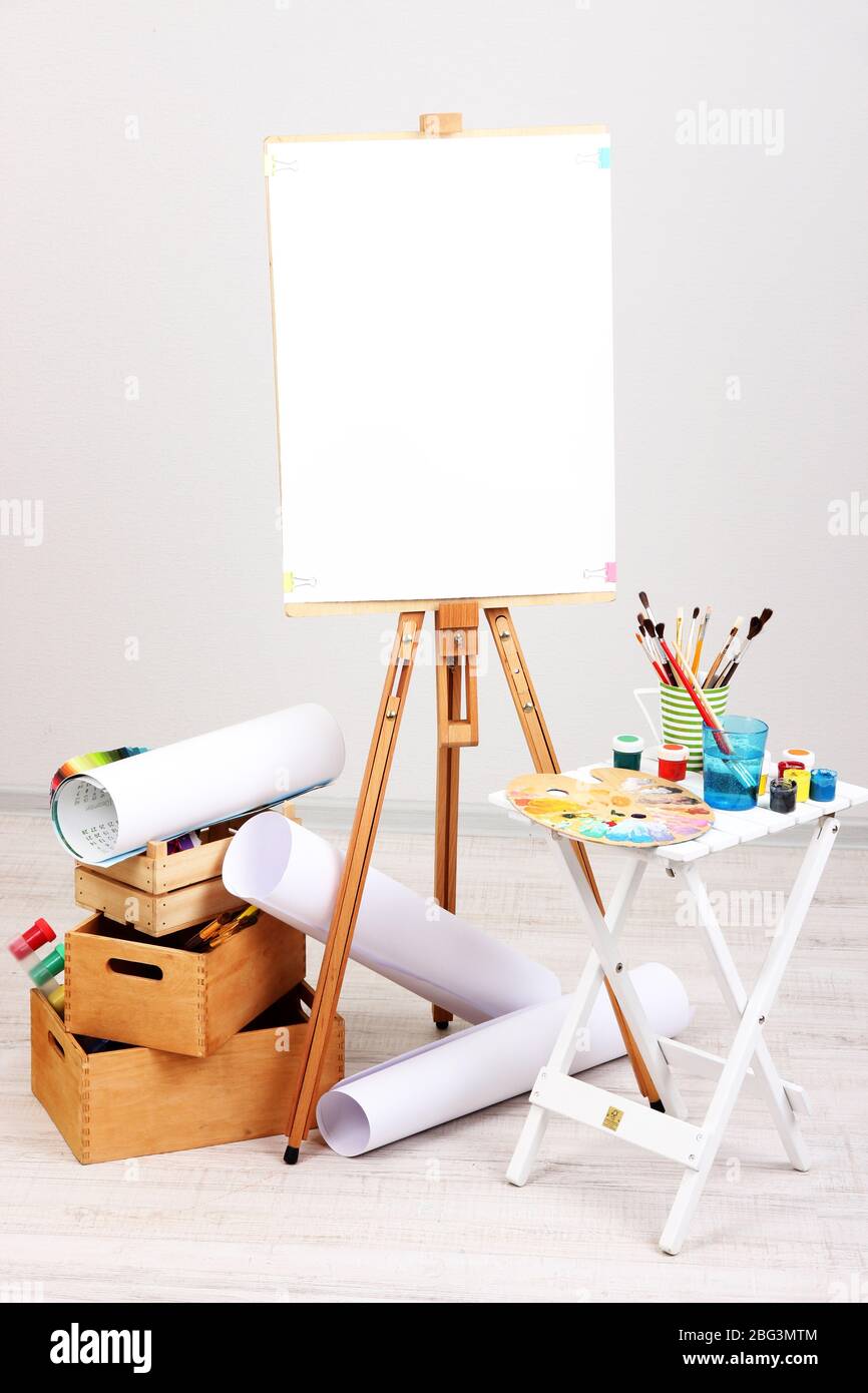 Wooden easel with clean paper and art supplies in room Stock Photo Alamy