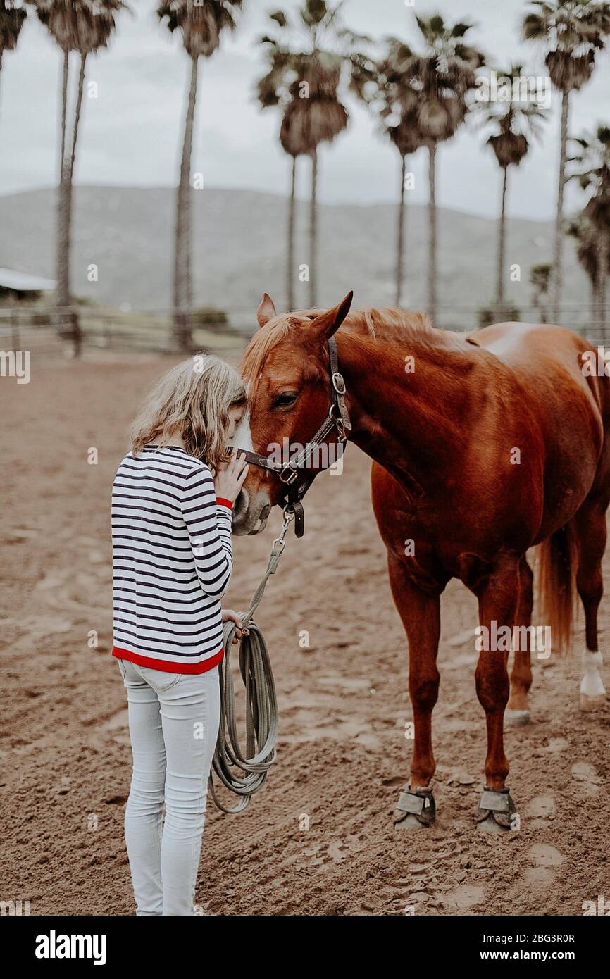 Girl standing on a ranch kissing a horse, California, USA Stock Photo