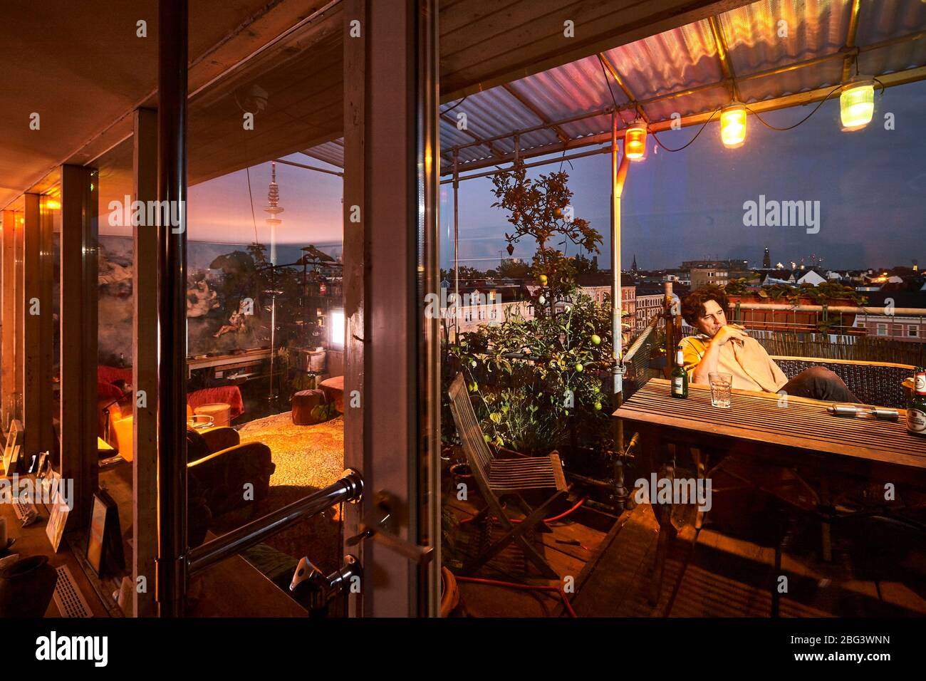 A man enjoys drinking a beer and smoking on his roof garden in the hip neighbourhood Sternschanze. Stock Photo