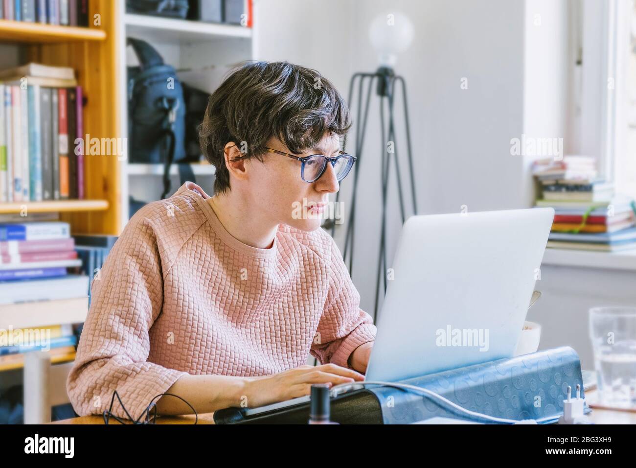 Woman working from home office. Young Caucasian short hair entrepreneur woman in sweater and glasses sitting and working online from home on computer Stock Photo